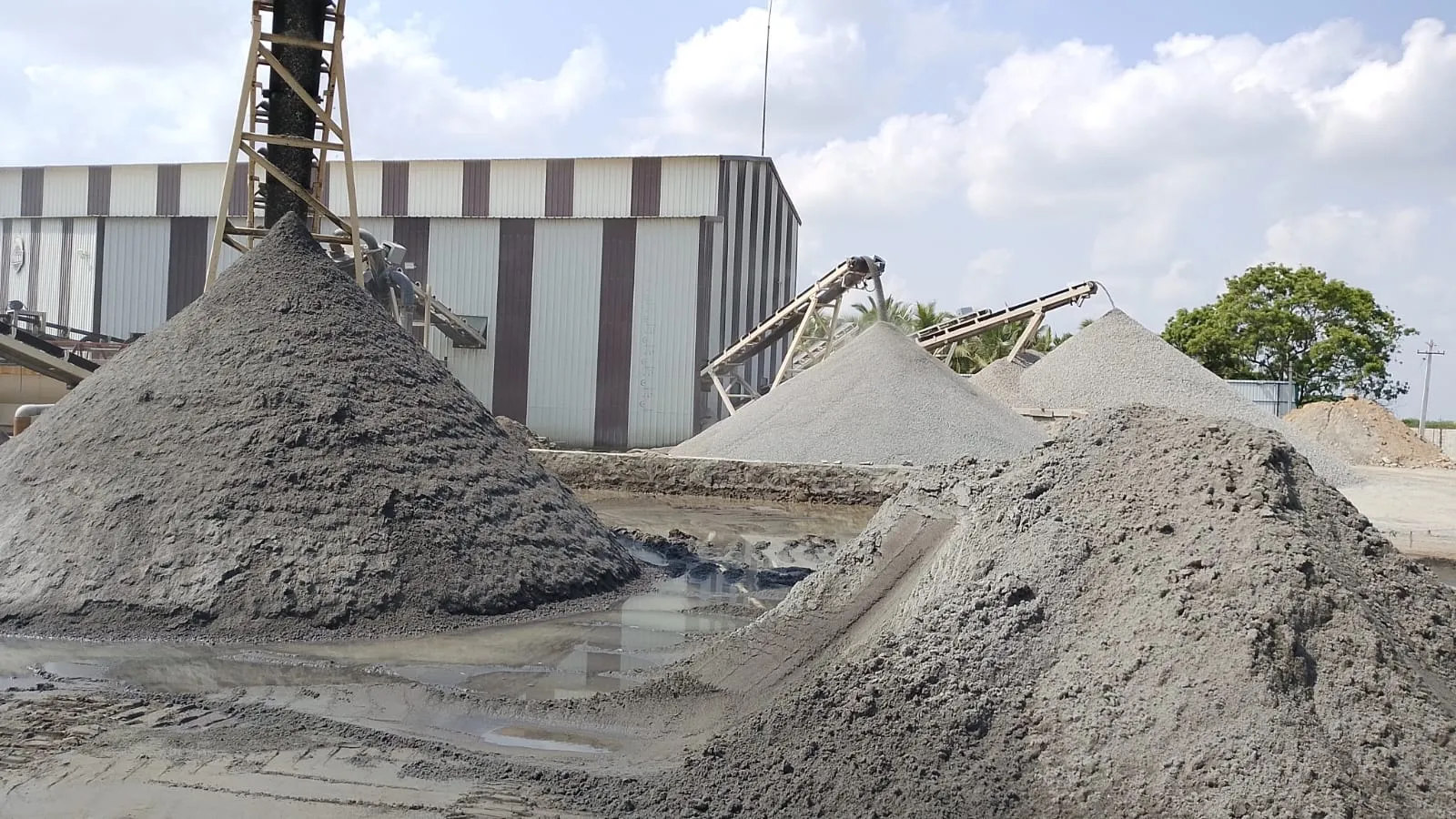 Large M-Sand and aggregate stockpiles on wet ground at Tirupati Balaji Blue Metals LLP facility, Virudhunagar, Tamil Nadu